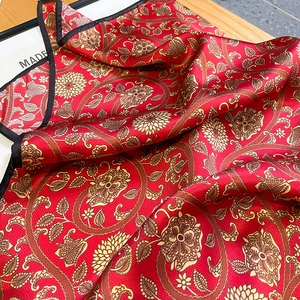 Close-up of red paisley silk scarf with gold patterns and black rolled edge details