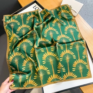 Deep green silk scarf with golden palm tree pattern displayed on a wooden surface