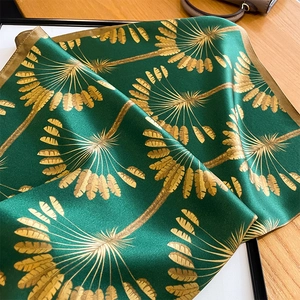 Detail of silk scarf with gold palm leaf print and premium stitched edges on wood surface