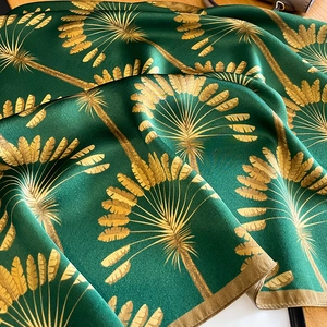 Detailed view of dark green silk scarf with golden palm leaf patterns on a wooden table