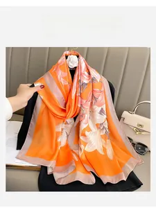 Close-up of a large silk scarf featuring orange lily floral patterns and pink edges