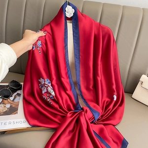 Elegant red silk scarf with floral print and blue borders draped on a beige sofa