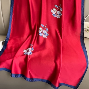 Elegant red floral silk scarf with navy blue borders and embroidery on leather surface