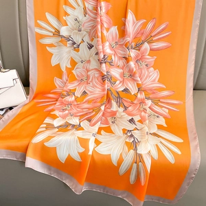 Elegant orange silk scarf with lily print draped over a sofa with a luxury bag