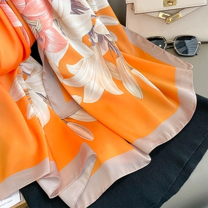 Detail of floral silk scarf with lily print and pink border next to accessories