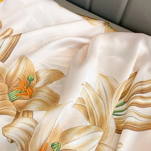Close-up of silk-textured fabric showing intricate orange lily floral patterns and luster