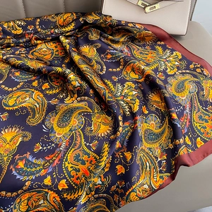 Navy blue paisley silk scarf with orange patterns and wine red borders on leather surface