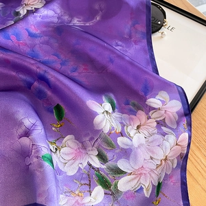 Purple mulberry silk scarf with magnolia print draped on a wooden desk with pearl accents
