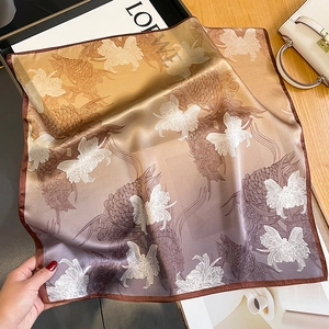 Elegant silk scarf with gradient koi and orchid patterns on a warm wooden tabletop