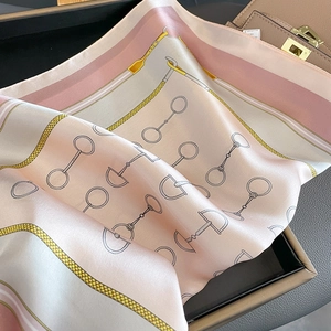 Silk square scarf with horse-bit pattern draped on a beige leather handbag