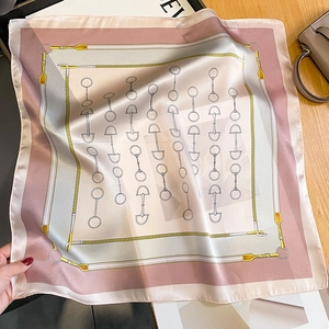 Elegant pink silk scarf with equestrian horsebit pattern on a stylish wooden tabletop