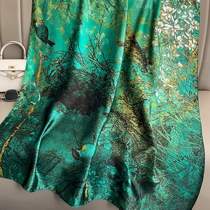 Green silk scarf with floral and bird prints draped on a sofa for a stylish summer look