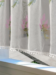Close-up of lavender embroidery on a semi-transparent white curtain with white pom-pom trim