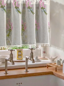 Detail of white cafe curtain with lavender embroidery and delicate pom-pom edge trim