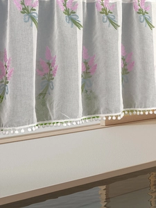 Detailed embroidery of lavender flowers and white pom-pom trim on semi-sheer door curtain