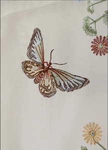 Detailed embroidery of a realistic butterfly with floral patterns on beige curtain fabric