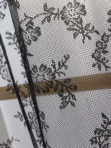 Macro detail of black lace curtain featuring delicate floral jacquard and hexagonal mesh