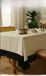 Detailed close-up of beige linen tablecloth with wide black lace trim on a wooden table