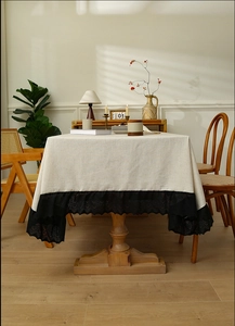 Detail of light beige tablecloth featuring elegant black floral lace trim and linen texture