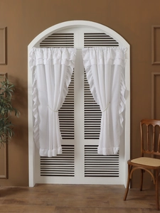 Close-up of white ruffle curtains with elegant pearl tiebacks on an arched window