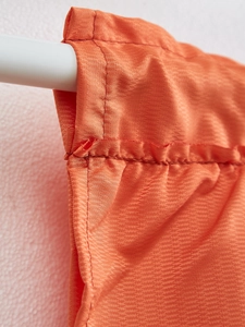 Detail of orange herringbone fabric curtain showing rod pocket top and precision stitching