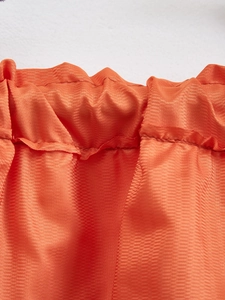 Close-up of orange retro cafe curtain featuring herringbone weave and ruffled elastic top