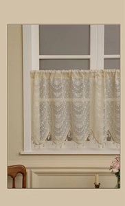 Dettaglio di tenda da caffè in pizzo crema vintage con motivi floreali e nappe eleganti