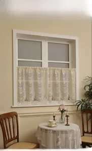 Dettaglio di tenda corta in pizzo color crema con motivi floreali e frange decorative