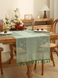 Macro detail of sage green floral lace table runner with fringe on a wooden dining table