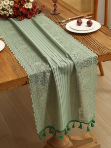 Detail of mint green lace table runner with hollow floral patterns and fringe edges
