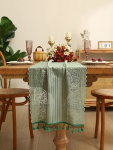Detail of sage green lace table runner featuring floral hollow patterns and tassel fringe