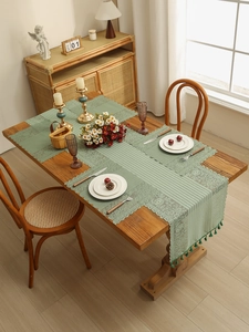 Detailed close-up of sage green lace table runner with hollow floral pattern and tassels