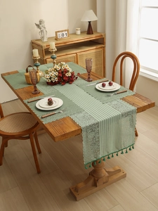 Detail of sage green lace table runner with floral embroidery and tassel fringe