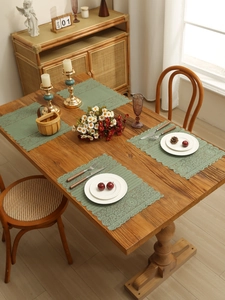 Close-up of four green lace placemats with hollow-out patterns on a rustic wooden table