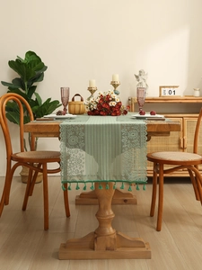 Detail of light green hollow lace table runner with floral embroidery and green tassels