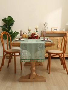 Detail of sage green lace table runner featuring floral hollow patterns and tassel fringe