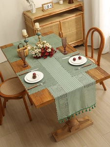Detail of sage green lace table runner with fringe trim on a rustic wooden dining table
