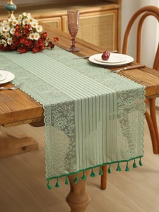 Detail of light green hollow lace table runner with fringe on a wooden table