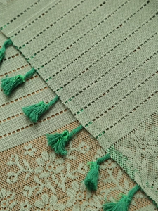 Close-up of sage green lace hollow knit runner with intricate floral patterns and tassels