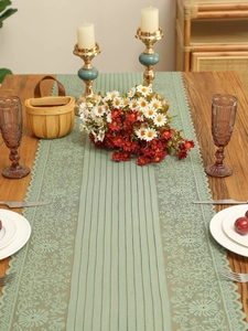 Macro detail of sage green hollow lace table runner with fringe on a wooden dining table
