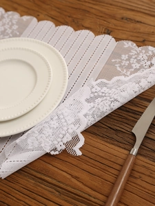 Close-up of white lace placemat with floral embroidery and wavy edges on wooden table