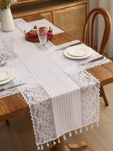 Detail of white lace table runner with intricate floral embroidery and tassel fringe decor