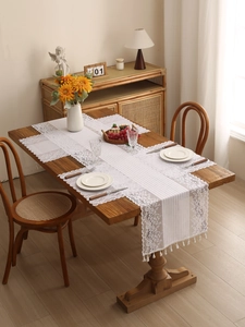 Detailed close-up of white lace table runner with floral hollow patterns and tassel fringe