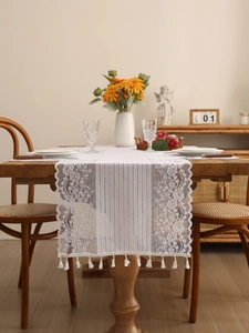 Detailed view of white floral lace table runner with fringe on a dark wood table