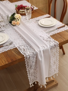 Close-up of vintage white lace table runner with floral embroidery and tassel details