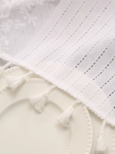 Close-up of white lace table runner featuring striped openwork and delicate fringe tassels