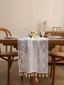 Close-up of white floral lace table runner with elegant tassels and hollow embroidery
