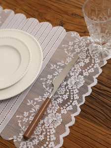 Detailed close-up of vintage hollow lace table runner with intricate fringe on dark wood