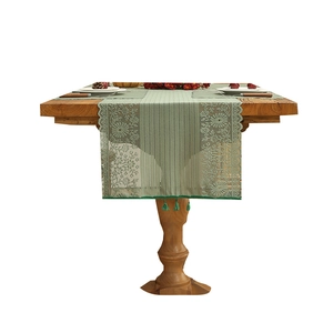 Green lace table runner with floral embroidery and tassels on a wooden dining table