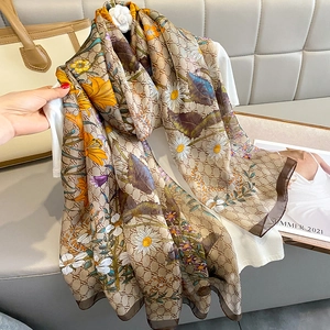 Elegant beige silk-like scarf featuring floral daisy patterns and repeat monogram prints